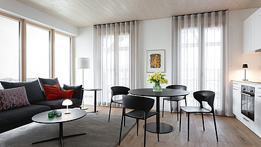 Foto eines möblierten Wohnraumes, des Holzgebäudes CARL in Pforzheim. Couch und Tisch mit Stühle.