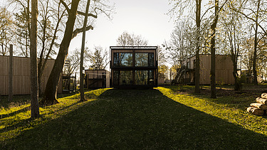 Photo of several small wooden houses with flat roofs. There are trees in the grounds.