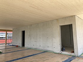 Photo of a wooden building shell. You can see an interior with a wooden ceiling and concrete wall.