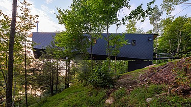 Photo of a wooden house on steel stilts in the middle of the forest.