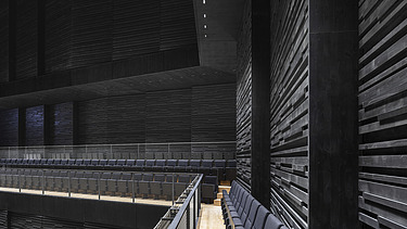 Foto eines Innenraumes der Interimsspielstätte Gasteig in München. Man sieht schwarze Akustikelemente aus Holz an den Wänden.
