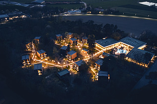 Foto einer Luftaufnahme bei Nacht. Man sieht beleuchtete Häuser und Bäume.