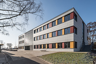 Foto einer Außenaufnahme der Schule Erfurt. Diese hat eine weiße, orange und rote Fassadengestaltung.