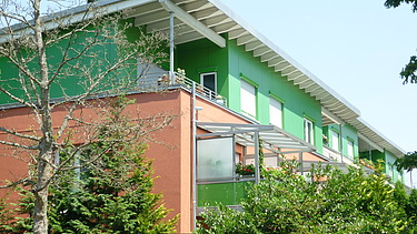 Foto eines mehrgeschossigen Gebäudes mit orange-grüner Fassade.