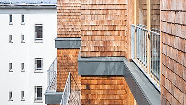 Foto einer mehrgeschossigen Wohnanlage aus Holz. Man sieht einen Detailausschnitt der Fassade aus Holzschindeln.
