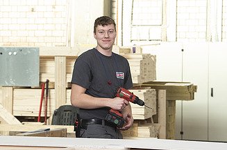 Karriere Ausbildung Zimmerer:Zimmerin ZÜBLIN Timber Foto eines jungen Auszubildenden Zimmerers, der in der Produktion steht und eine Bohrmaschine hält.