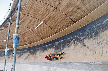 Foto von einer Rodelbahn mit Holzüberdachung und einem liegenden Bobfahrer