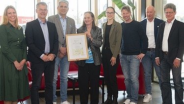 News ZÜBLIN Timber Photo with eight people. A woman holds the Holz von Hier certificate for the new ZÜBLIN Timber office building.