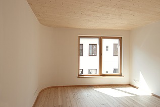Foto eines Wohnhauses aus Holz. Detailbild unmöbliertes Wohnzimmer mit sichtbarer LENO-Holzdecke.