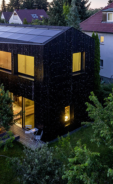 Foto eines Wohnhauses aus Holz und mit dunkler Holzfassade. Abendstimmung.