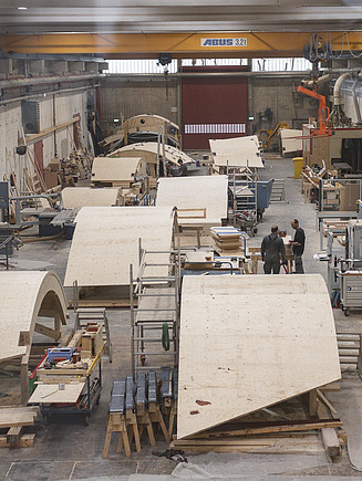 Foto von gebogenen Holzelementen für die Rodelbahn Thüringen. Diese liegen in der Werkshalle von ZÜBLIN Timber.