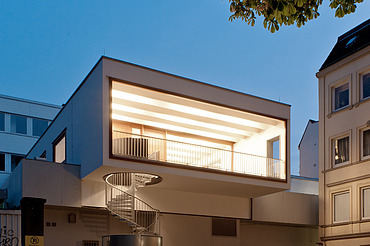 Night shot of a building with external spiral staircase. Wooden extension.