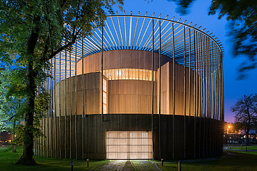 Foto des Elizabethan Theatres in Condette Frankreich. Zu sehen ist ein rundes Holzgebäude bei Nacht.