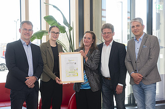 Aktuelles ZÜBLIN Timber Foto mit fünf Personen. Zwei halten das Zertifikat Holz von Hier für den Büroneubau von ZÜBLIN Timber.
