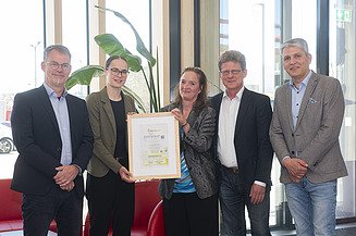 Photo with five people. Two are holding the Holz von Hier certificate for the new ZÜBLIN Timber office building.