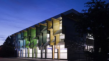 Night shot of a school building with colorful façade elements made of laminated veneer lumber.