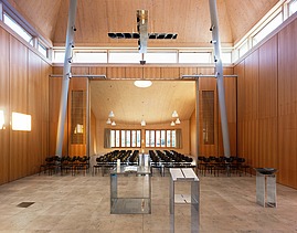  Foto der Kirche Burgweinting von innen. Zu sehen ist ein bestuhlter Innenraum und viele Holzoberflächen.