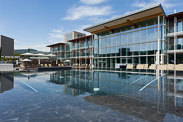 Foto des Hotels Aqualux ini Bardolino. Zu sehen ist ein großes Gebäude mit Glasfassade und Flachdach, zudem ein Pool.