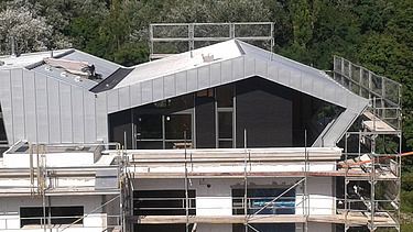 Foto eines Ausschnittes eines mehrgeschossigen Gebäudes. Man sieht eine Aufstockung aus Holz.