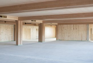 Foto eines Innenraumes der Baustelle Schule am Hang. Zu sehen sind LENO-Brettsperrholzoberflächen und BauBuche-Stützen.