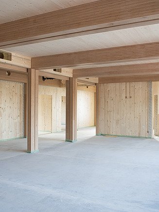 Photo of an interior of the construction site school on a slope. LENO cross-laminated timber surfaces and BauBuche supports can be seen.