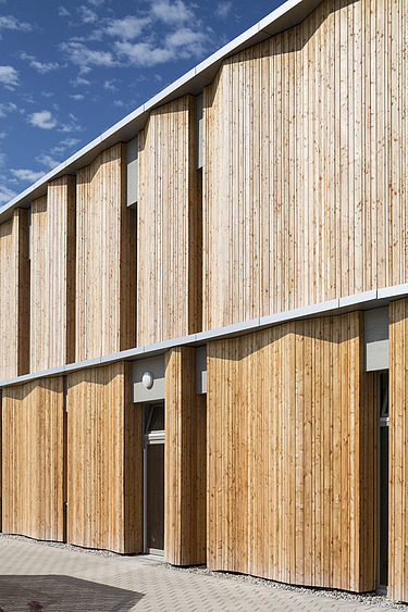 Exterior photo of the Campeon Infineon daycare center in Neubiberg. You can see a section of the building and the wooden façade.