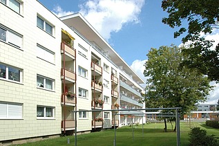 Photo of a multi-storey building with garden in front. Wooden extension.