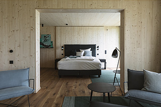 Foto eines Wohnraumes von Innen. Bett, Stühle und Holzwände.