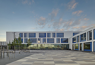 Außenaufnahme des Gymnasiums München-Nord. Man sieht ein großes, weißes Gebäude mit Flachdach.