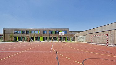 Photo of a wooden school from the outside. You can see the wooden building and the sports field.