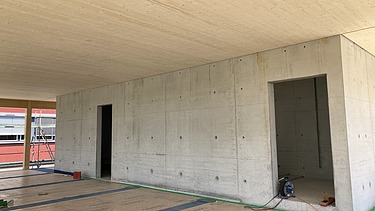 Foto eines Rohbaus aus Holz. Man sieht einen Innenraum mit Holzdecke und Betonwand.
