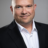 Contact finder Martin Schimpf Photo of a smiling man with a bald head, black jacket and white shirt
