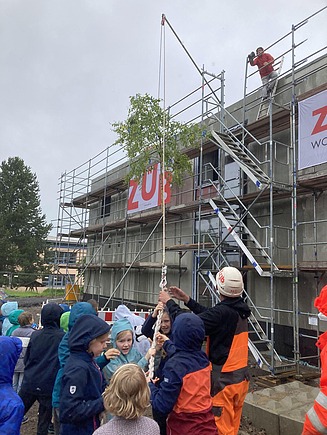 Foto vom Richtfest Schule Emleben mit Kindern und Menschen vor dem MOLENO-Gebäude. Der Richtbaum wird gerade hochgezogen.