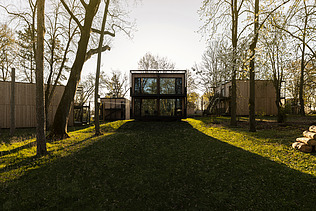 Photo of several small wooden houses with flat roofs. There are trees in the grounds.