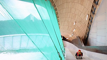 Photo of a bobsleigh run with a wooden roof and a lying bobsleigh rider in red clothing