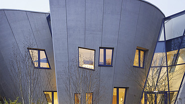 Photo of a building with a wooden façade and sloping walls. Picture at dusk.