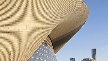 Photo of the Aquatics Center in London from the inside. You can see the wooden roof construction and a large swimming pool.