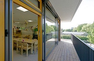 Innenaufnahme der Kita in Frankfurt. Man sieht eine Terrasse und durch ein geöffnetes Fenster einen Aufenthaltsraum. 