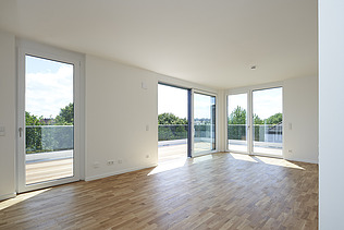 Photo of a bright, empty interior with white walls and wooden floor.