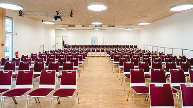 Photo of a lecture hall furnished with red chairs at Witten University. You can see a large wooden ceiling. 