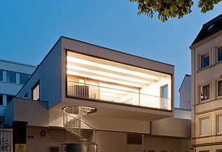 Night shot of a building with external spiral staircase. Wooden extension.