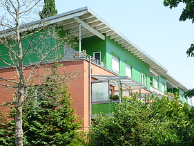 Foto eines mehrgeschossigen Gebäudes mit orange-grüner Fassade.