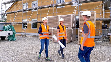 Foto von einem Projektleiter, der mit einer Kollegin in einem Rohbau aus Holz steht