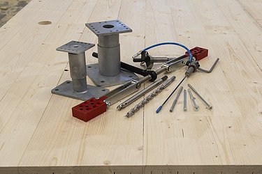 Photo of various tools and fasteners from ZÜBLIN Timber. These are placed on a LENO panel.