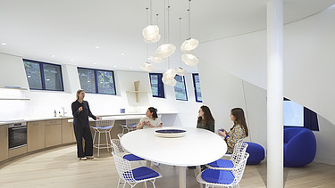 Photo of a recreation room. Four women are in the room. Three are sitting, one is standing.