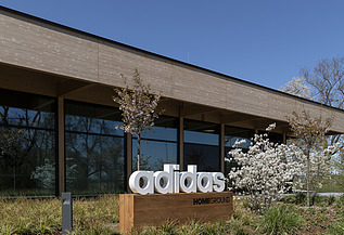 Photo of a building with a flat roof. In front of it is a sign with the inscription adidas
