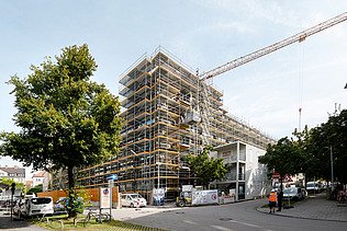 Foto des Rohbaus VINZENT in München. Zu sehen ist ein eingerüstetes, mehrgeschossiges Gebäude.