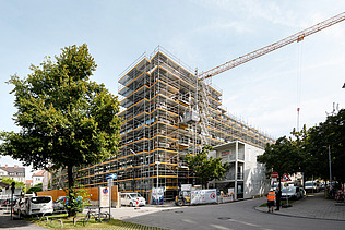 Photo of the VINZENT building shell in Munich. You can see a scaffolded, multi-storey building.