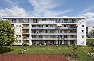Foto eines mehrgeschossigen Gebäudes mit Garten und Hartplatzfeld davor. Aufstockung aus Holz.