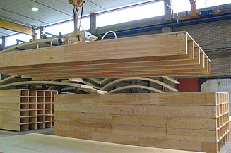 Foto von eines Rippenelements am Kran in der Produktionshalle von ZÜBLIN Timber. Man sieht auch Kastenelemente.